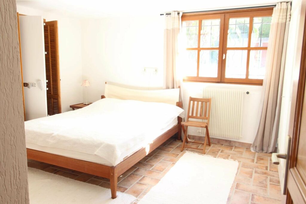 bedroom with white bedding and wooden windows facing garden