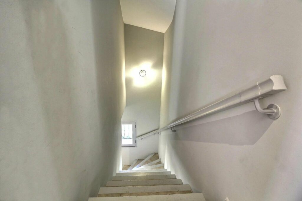 hallway leading down with white tile stairs and white walls