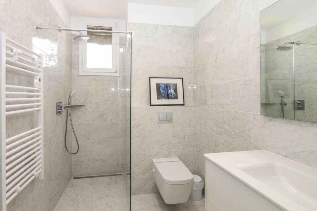 bathroom with large standing shower and light grey tiling