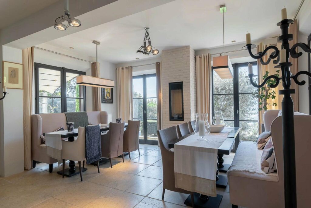 chic dinning room with beige tile floors and large french door windows and hanging metal light fixtures