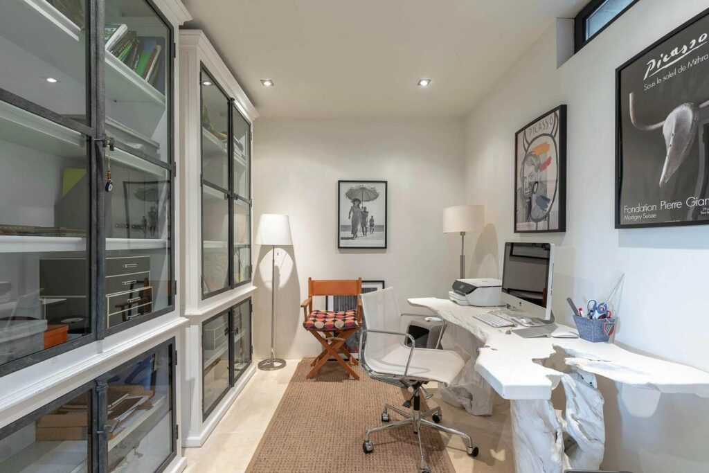 office with glass fram shelves filled with books and white large desk area