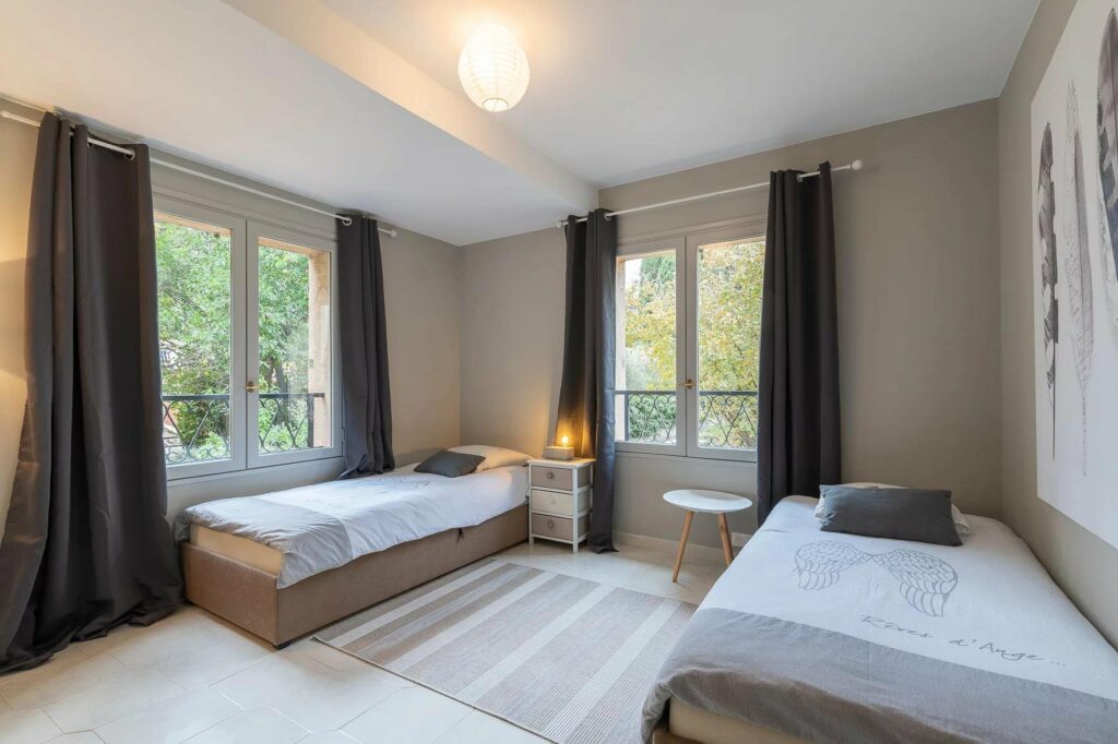 bedroom with two single beds with grey rug in center and large french door windows with view of garden