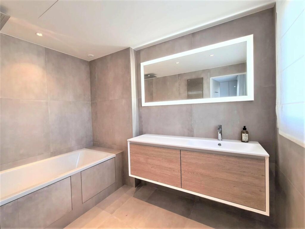 bathroom with bathtub and light grey tiling and brown wooden vanity