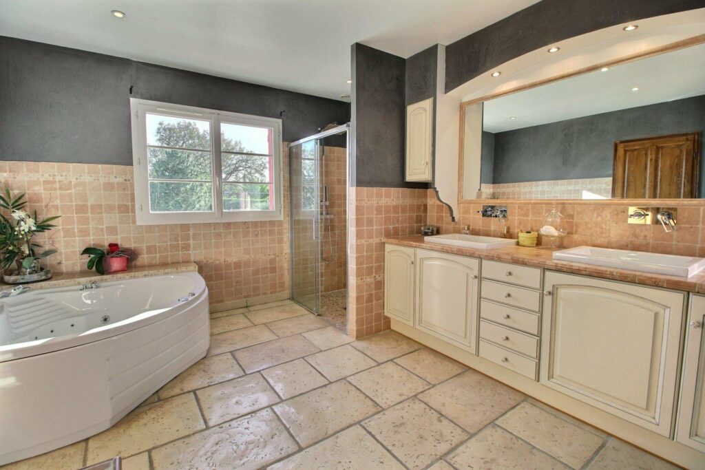 bathroom with beige tile and beige cabinets and window with view of the garden