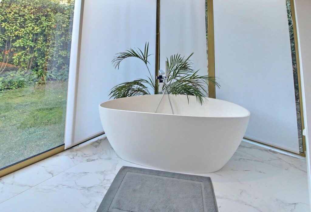 bathroom bathtub with marble floors and glass walls with view of garden