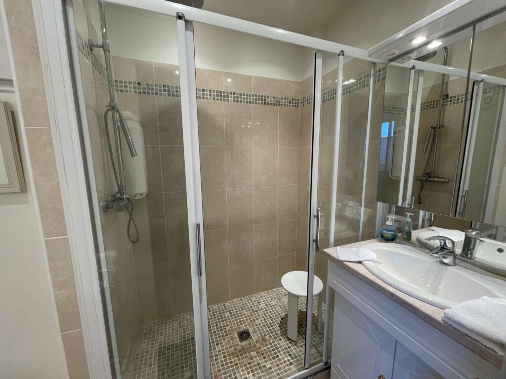 bathroom with beige tiling and large standing glass shower with white sink