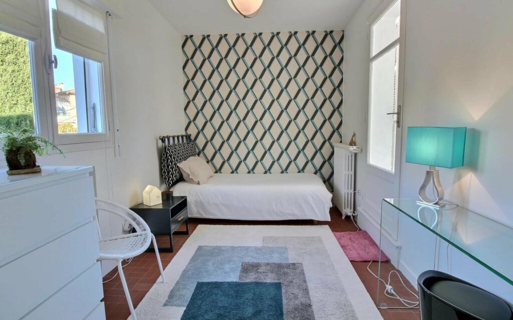 bedroom with green and white pattern wallpaper and small white bed in corner
