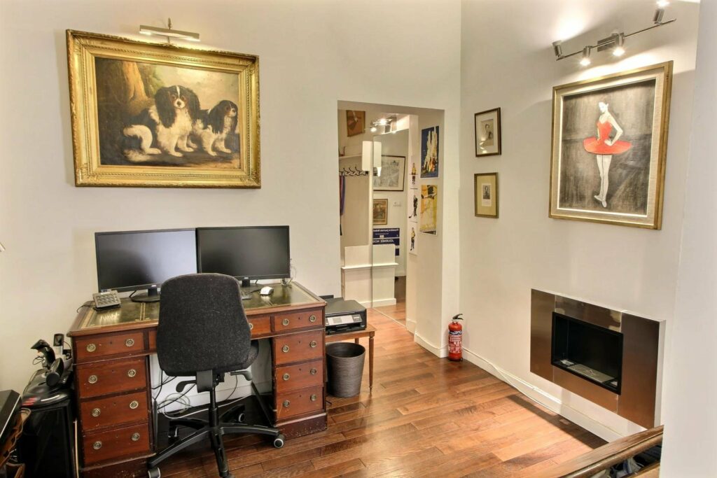 office with wooden desk area with white walls filled with classical paintings