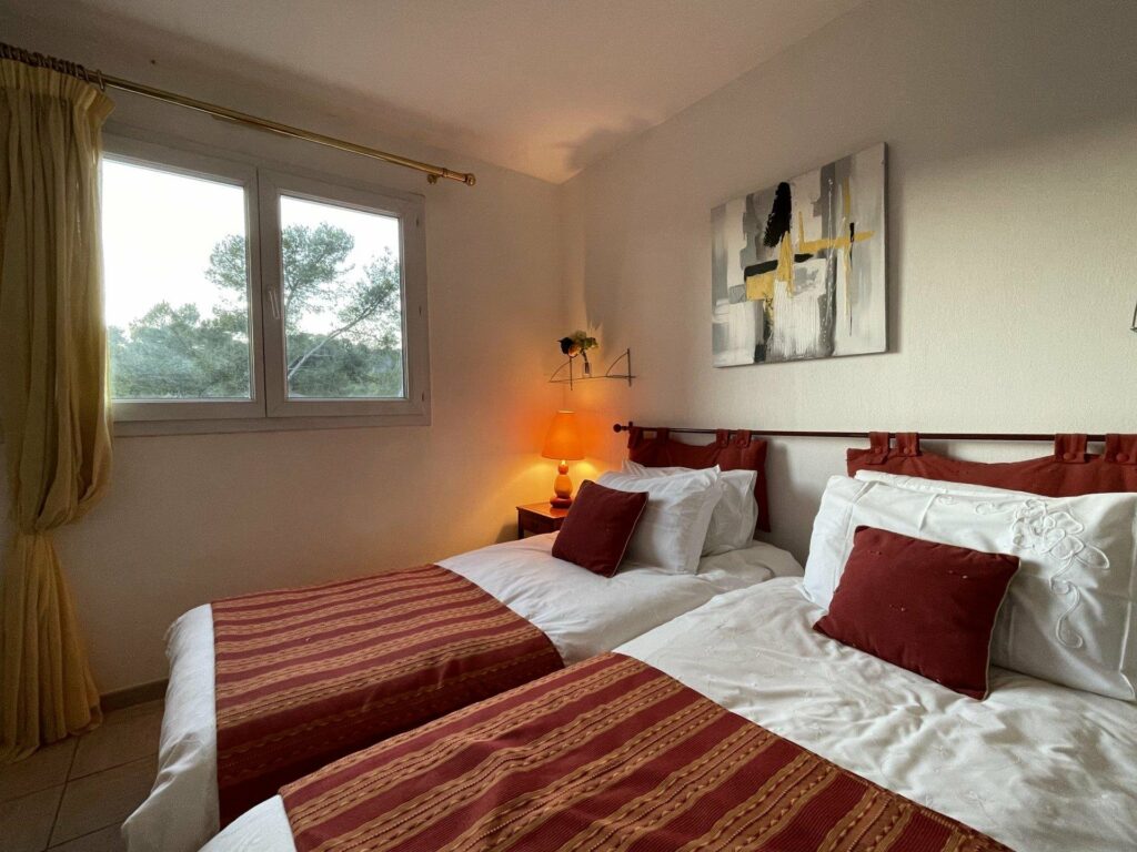 bedroom with two single beds with white and red bedding and small room with view of garden