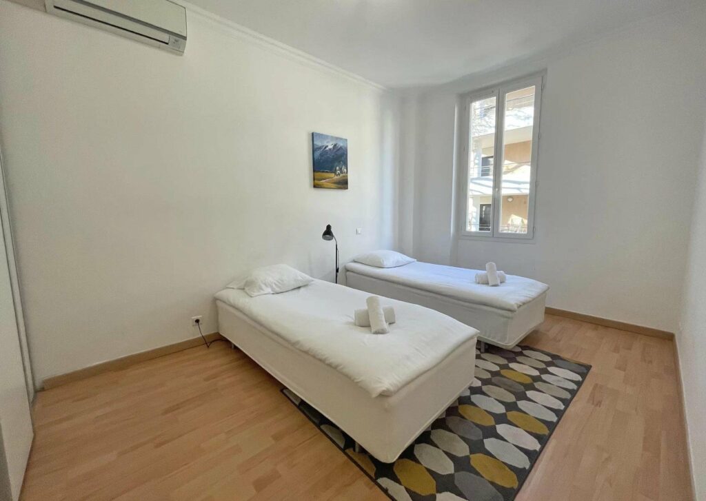 bedroom with 2 single beds and wooden floors next to small window with view of city