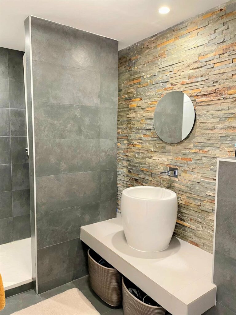 bathroom with grey tile walls and white sink with small round mirror