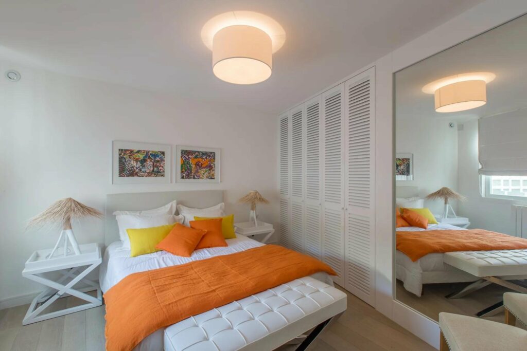bedroom with white and orange bedding and small beige chandelier hanging above it