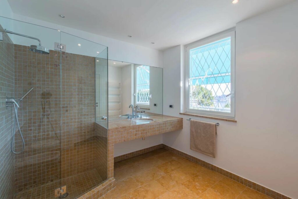 bathroom with beige tile sink area and standing glass shower with brown tile floors