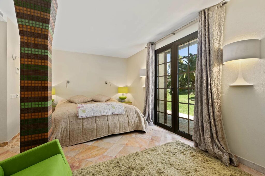 bedroom with beige bedding and tile floors with wooden door to backyard garden