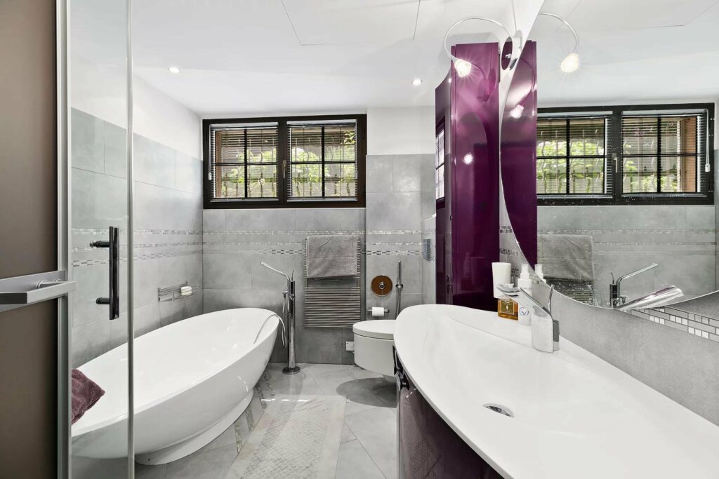 bathroom with grey tile walls and floors and white bathtub
