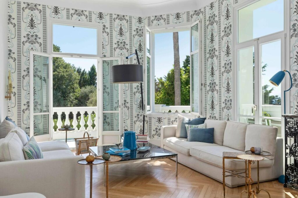 living room in south of france with blue and white printed wallpaper and long white couch and blue accent pillows