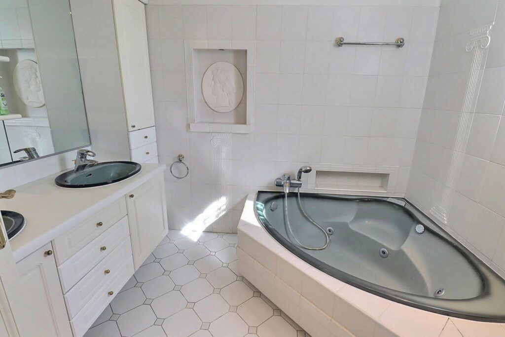 bathroom with grey jacuzzi in corner and small double sink with white cabinets