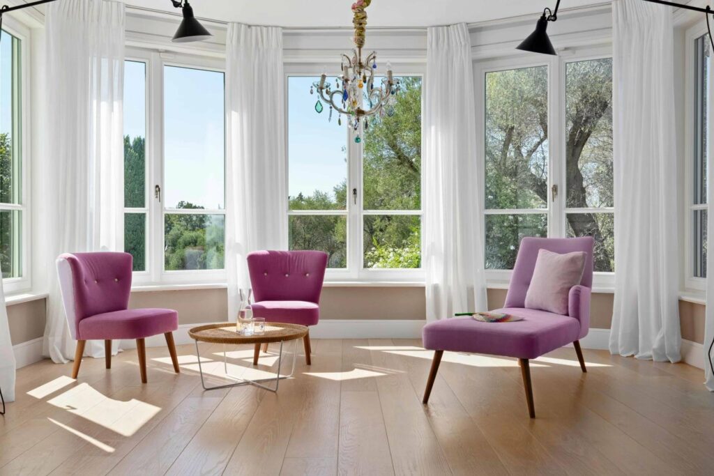 seating area with purple chairs and metal chandelier in center and large corner windows with garden view
