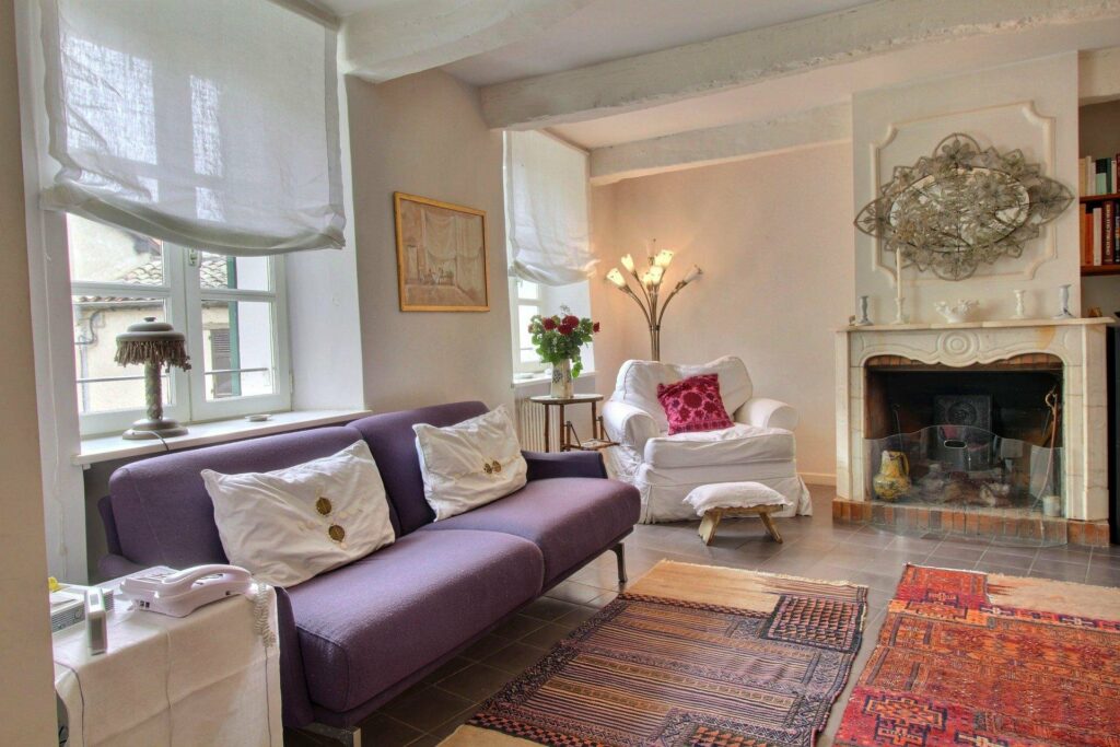 living room with purple couch and printed rug underneath and white couch in corner