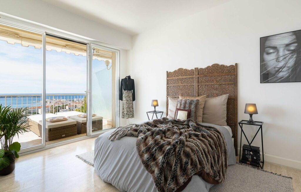 bedroom with queen size bed with brown fur blanket and access to terrace with sea view