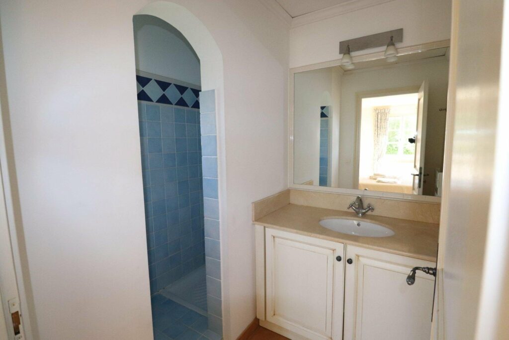 white bathroom with white cabinets and secluded blue shower area