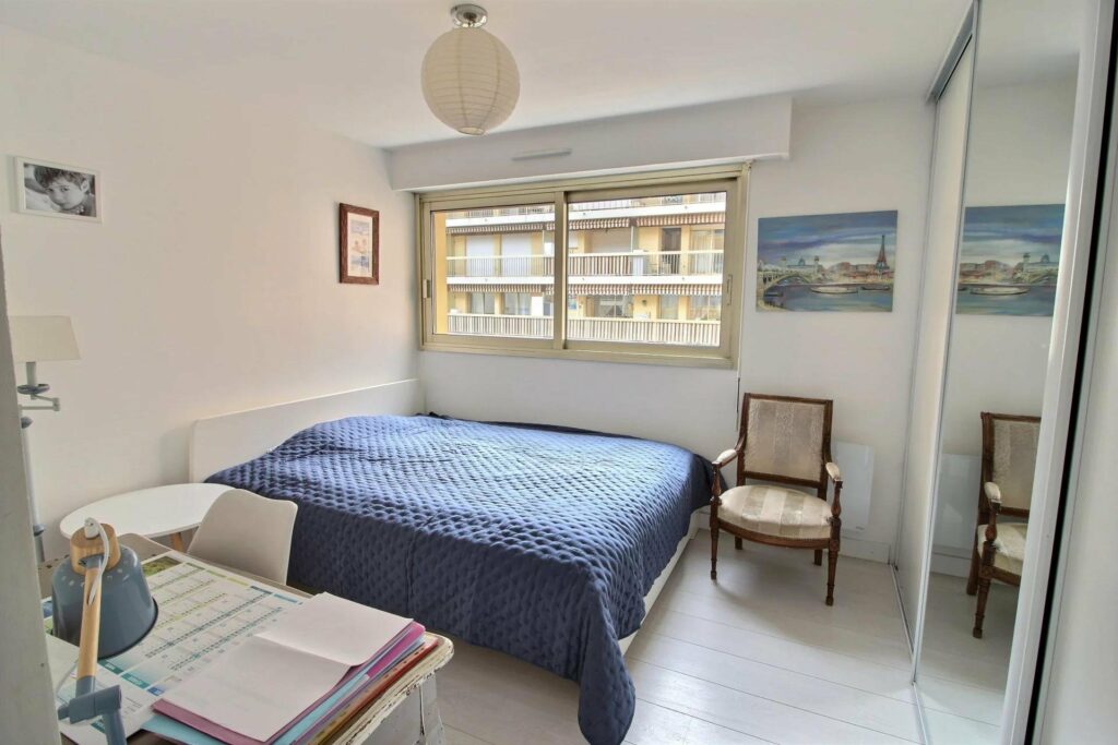 bedroom with queen size bed with navy bedding under small window with view of city