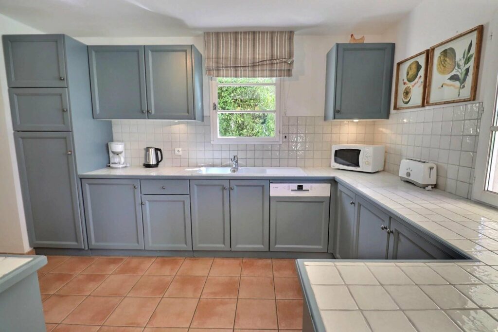 kitchen with pale blue cabinets and small window with garden view above sink