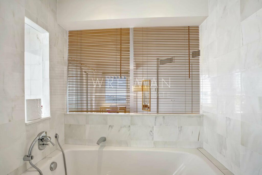 bath tub next to sea view window with wooden blinds