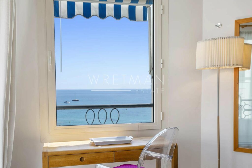 wooden desk with pink plastic chair facing window with sea view in cannes