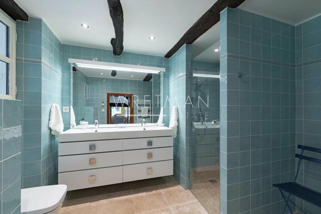 bathroom with blue tiling and large shower and white cabinets