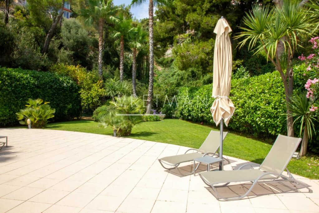 large backyard garden with two sun chairs and one umbrella