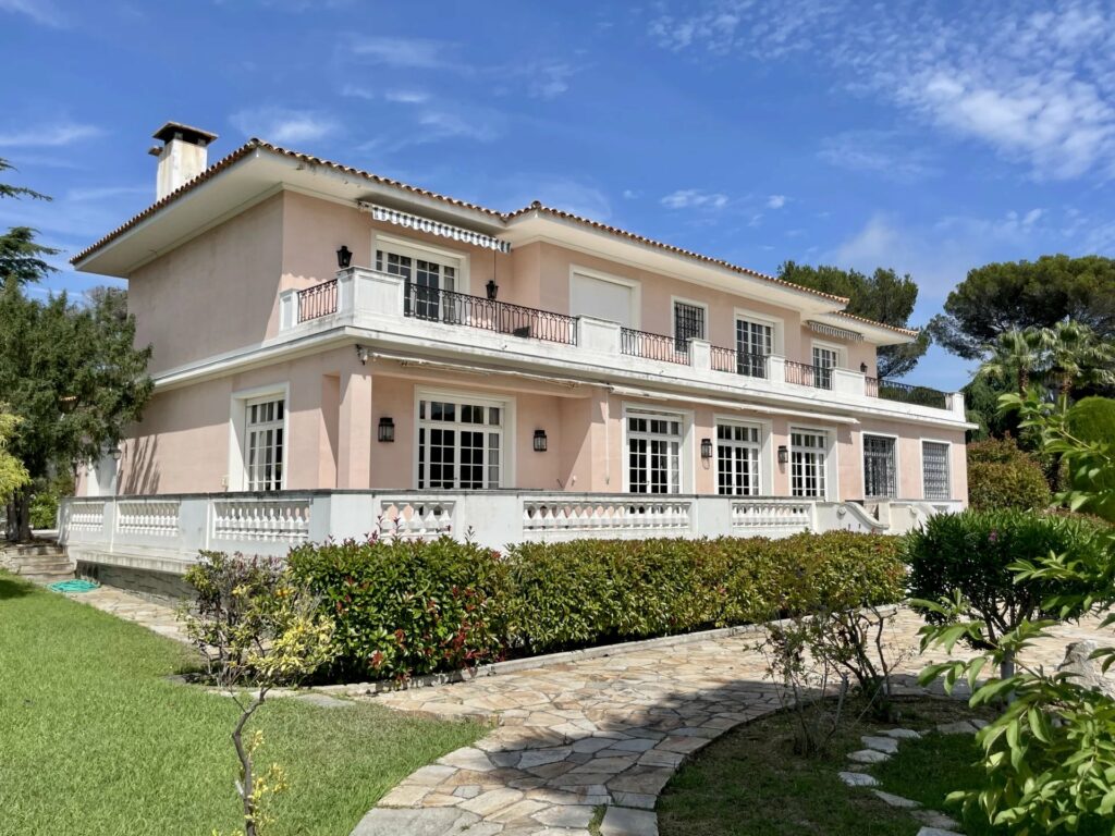 two storey villa that is light pink and surrounded by garden
